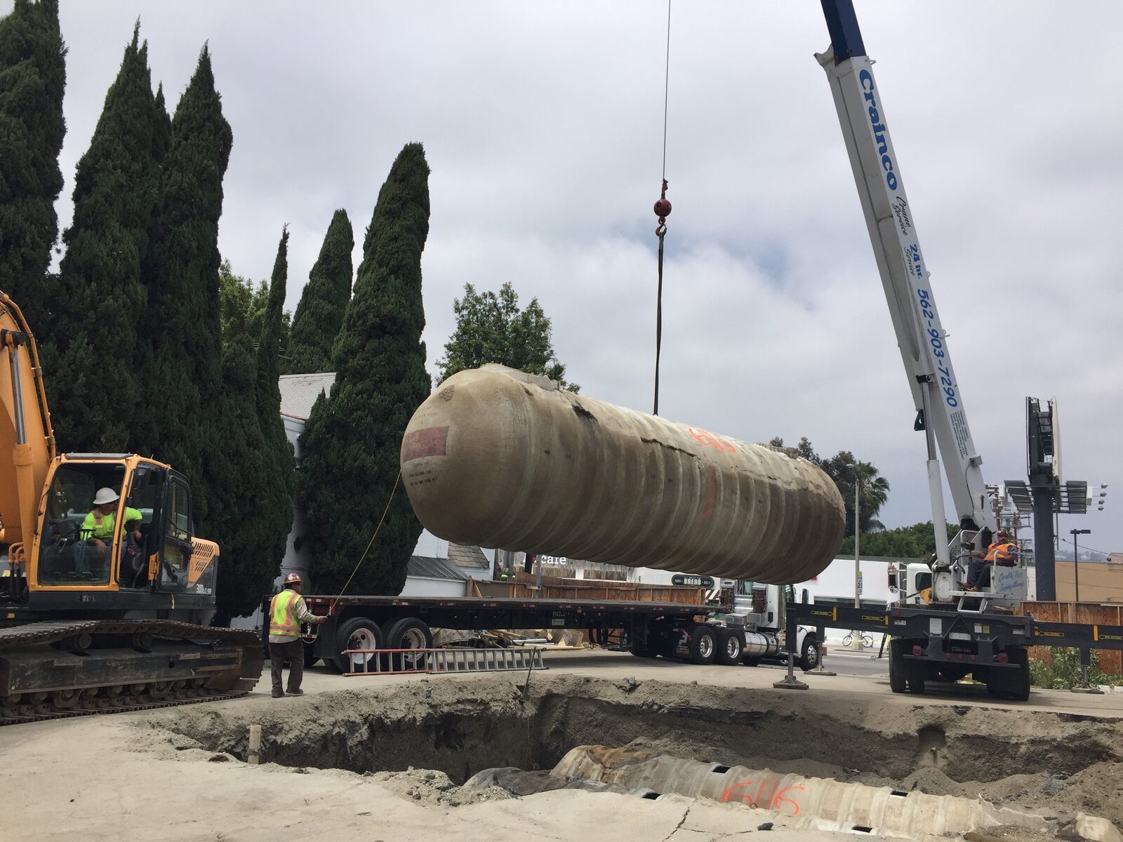 A crane lifts a 25,000-gallon underground storage tank out of an excavation while field staff observe from the site perimeter.