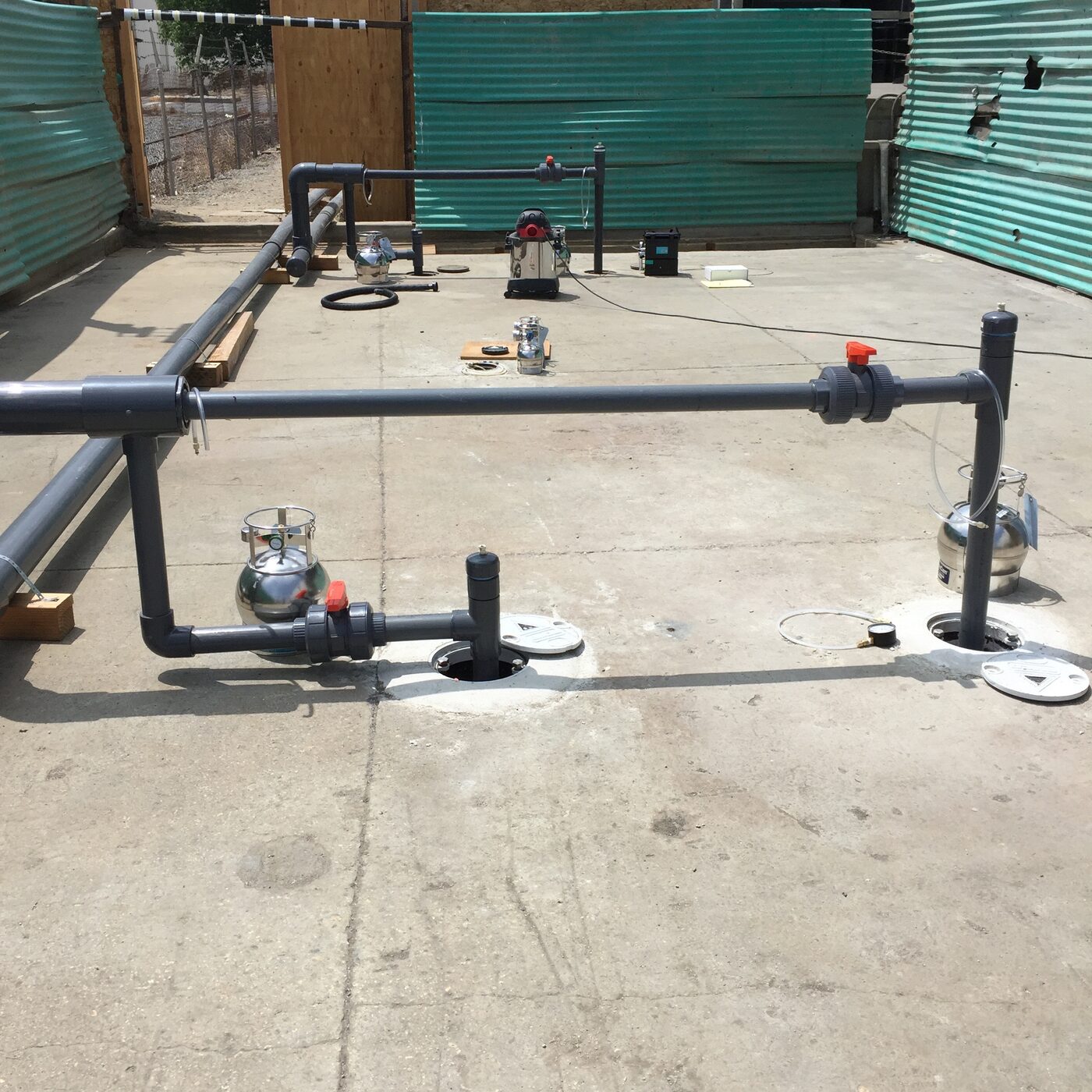 Vapor extraction wellheads and summa canisters connected by grey manifold piping across a concrete pad at an active remediation site.